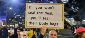 A protester holds a sign reading, "If you won't seal the deal, you'll seal their body bags," during a nighttime demonstration.